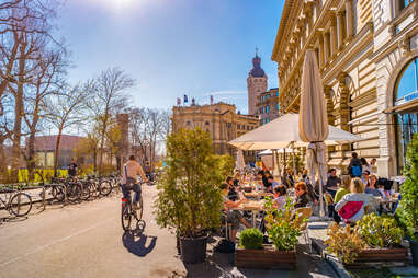 person riding bike past busy outdoor cafe in leipzig, germany